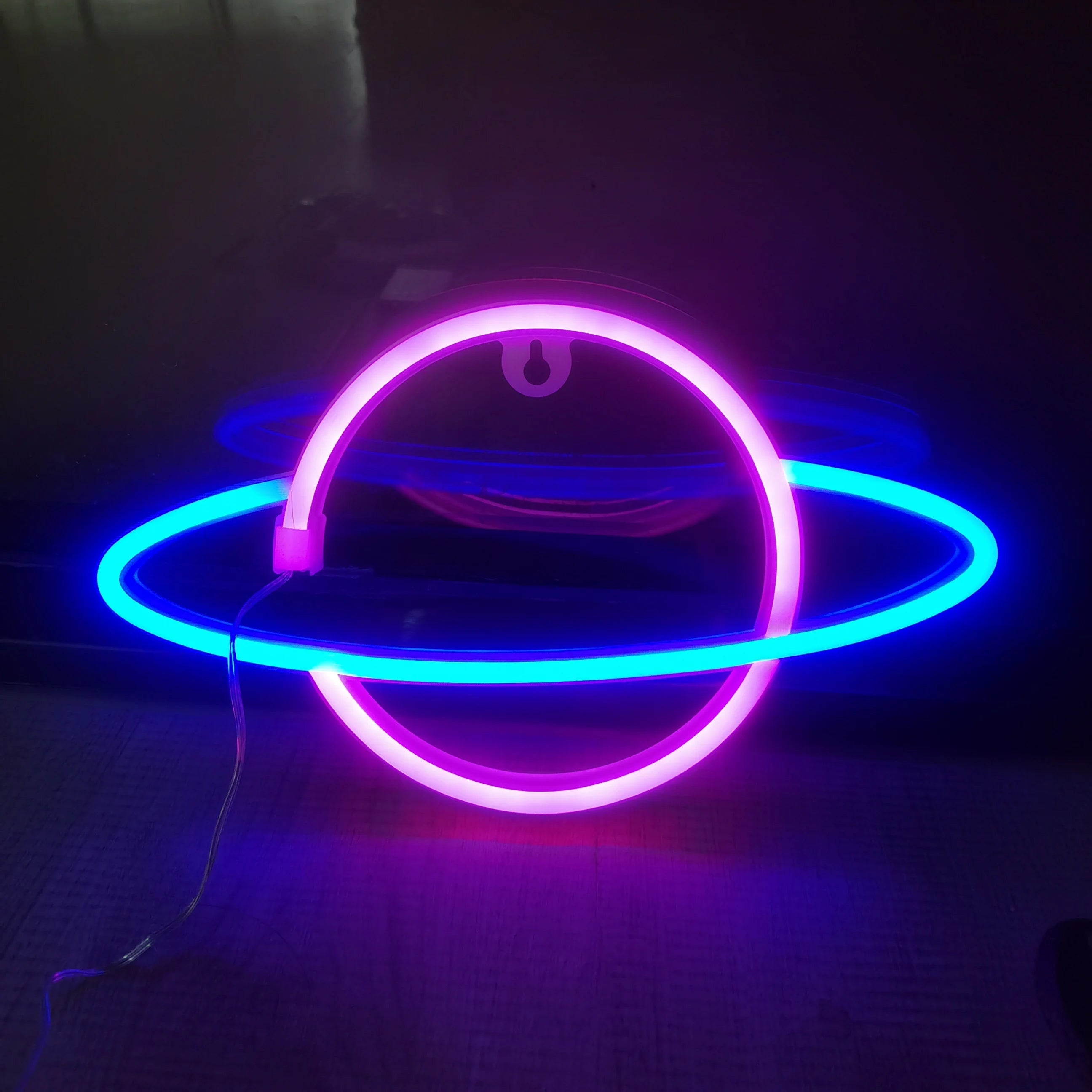 Neon sign shaped like a planet with pink and blue rings on a dark background